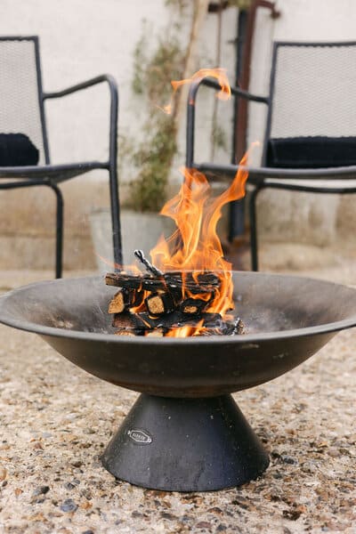 A wood fire lit in a cast-iron fire pit on the terrace at Amelia's Ojas Sauna, with seating for guests to warm up around it