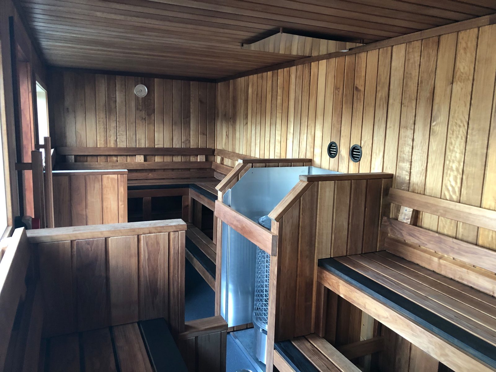 Inside a 20ft container sauna: benches on two levels down the whole length, the heater in a wooden guard