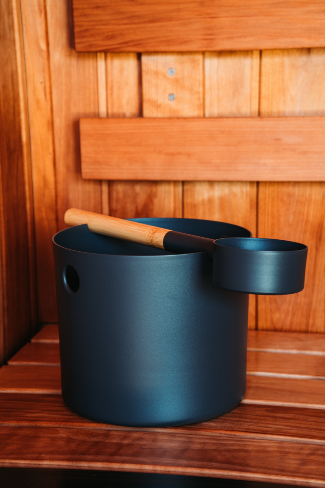 Matte black sauna bucket and ladle resting on a cedar bench inside a container sauna