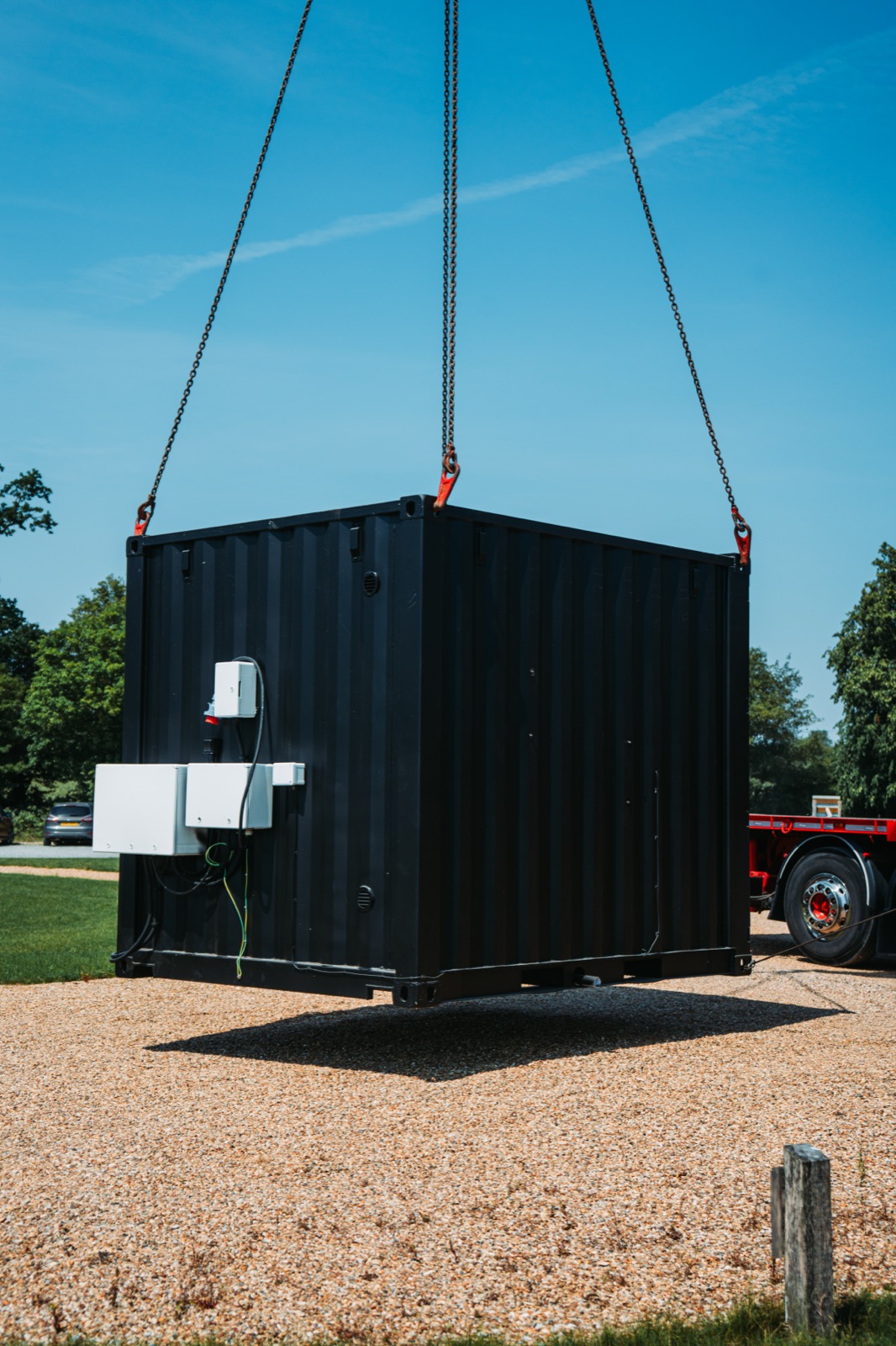 A black container sauna being lowered by crane onto site on delivery day