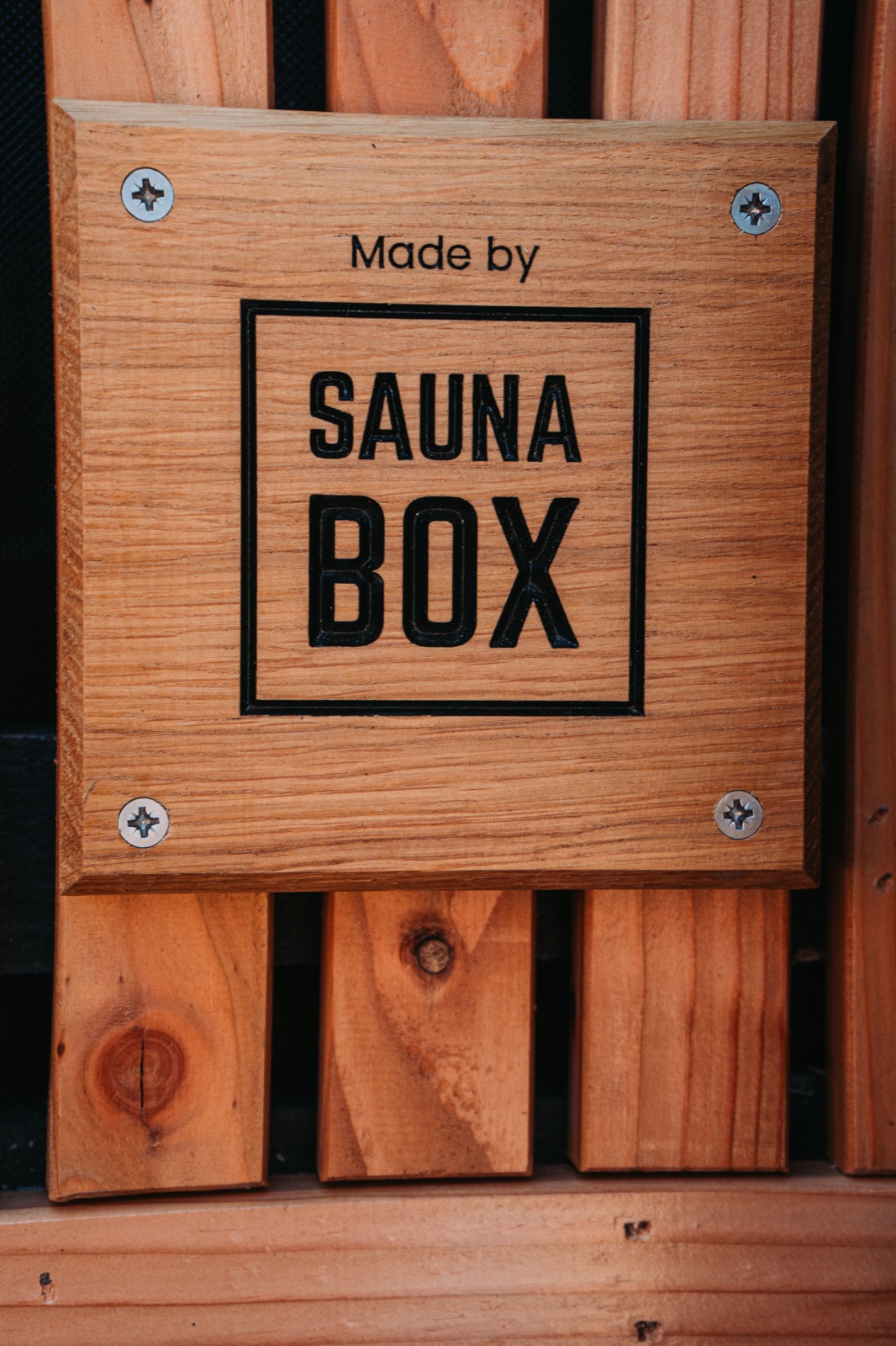 A "Made by Sauna Box" wooden plaque on the cedar interior of a container sauna
